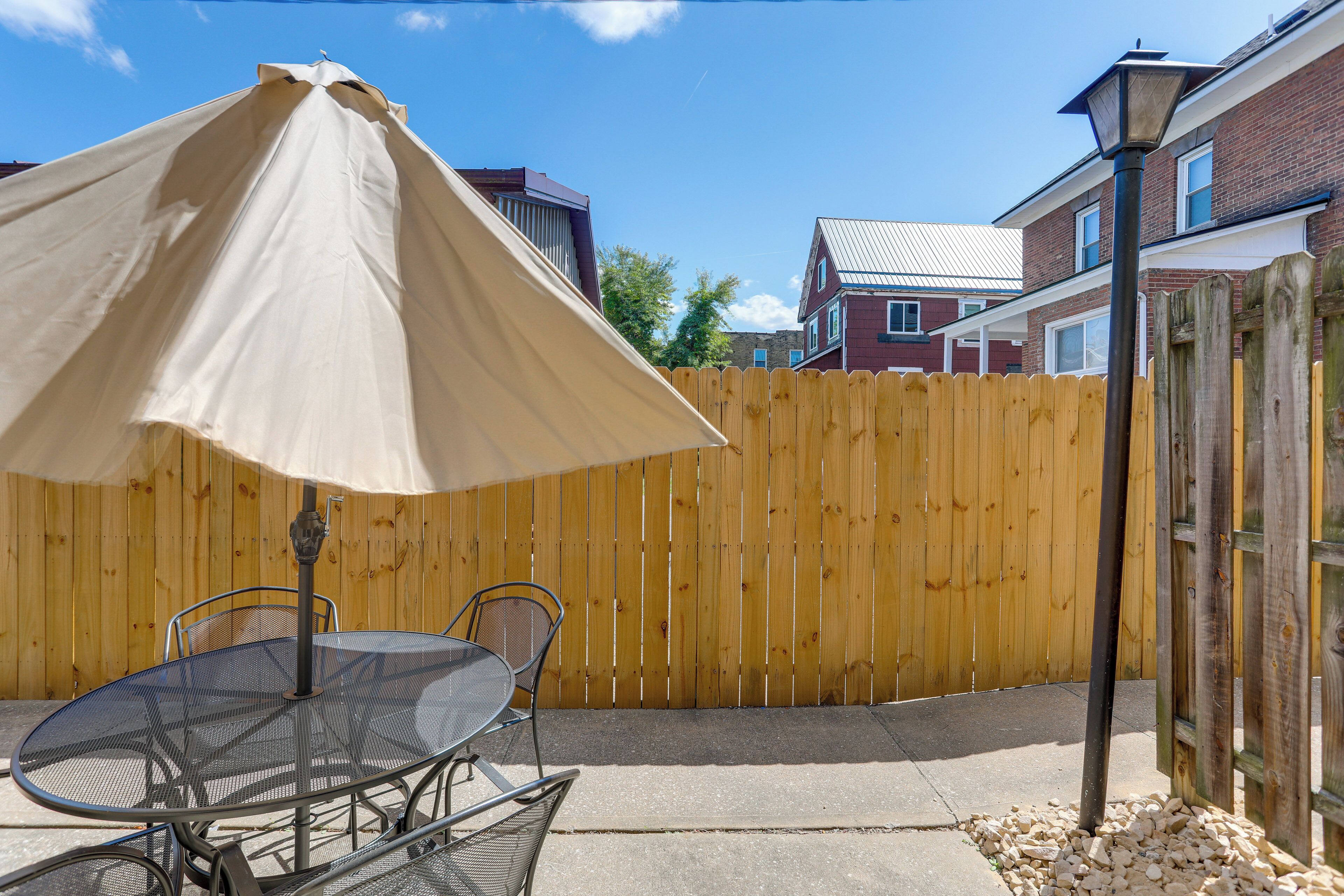 A patio with a metal table and chairs, a beige umbrella, and a wooden fence.