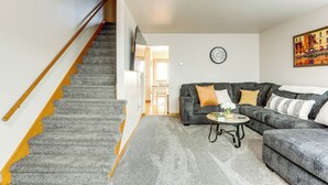 Un salon avec un tapis gris, un canapé gris, une table basse ronde et un escalier doté de rampes en bois.