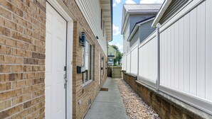 Un étroit passage entre deux maisons en briques, avec une porte blanche sur le côté gauche et une clôture blanche sur le côté droit.