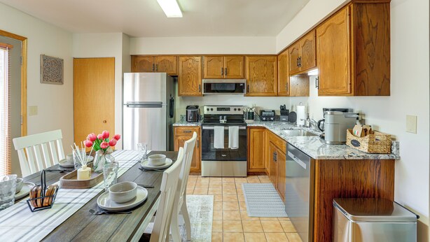 Une cuisine moderne avec des meubles en bois, des appareils en acier inoxydable et un coin repas avec une table dressée pour quatre personnes.