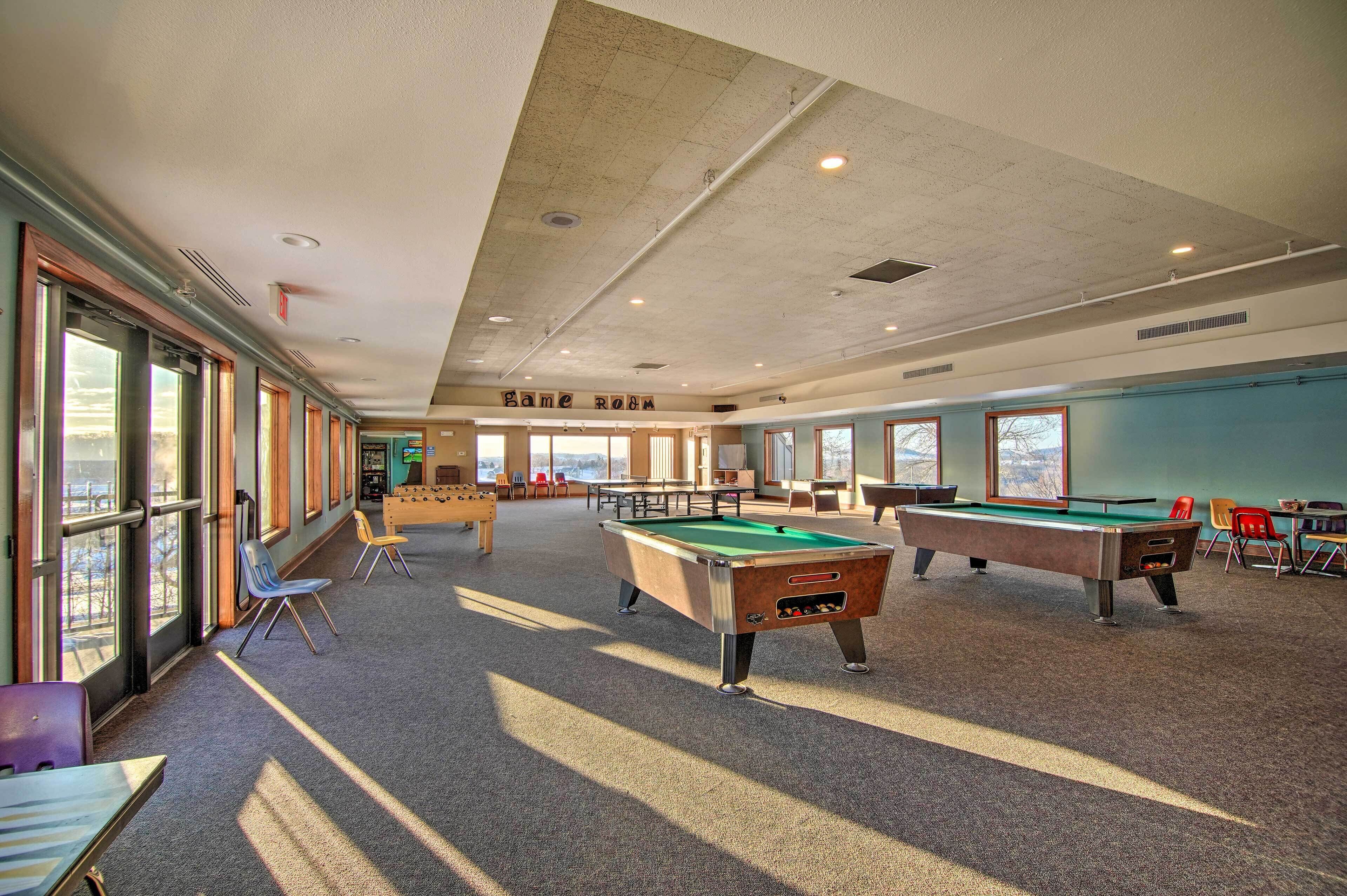 A pool table area with multiple tables and chairs, large windows, and a ceiling with visible ductwork.