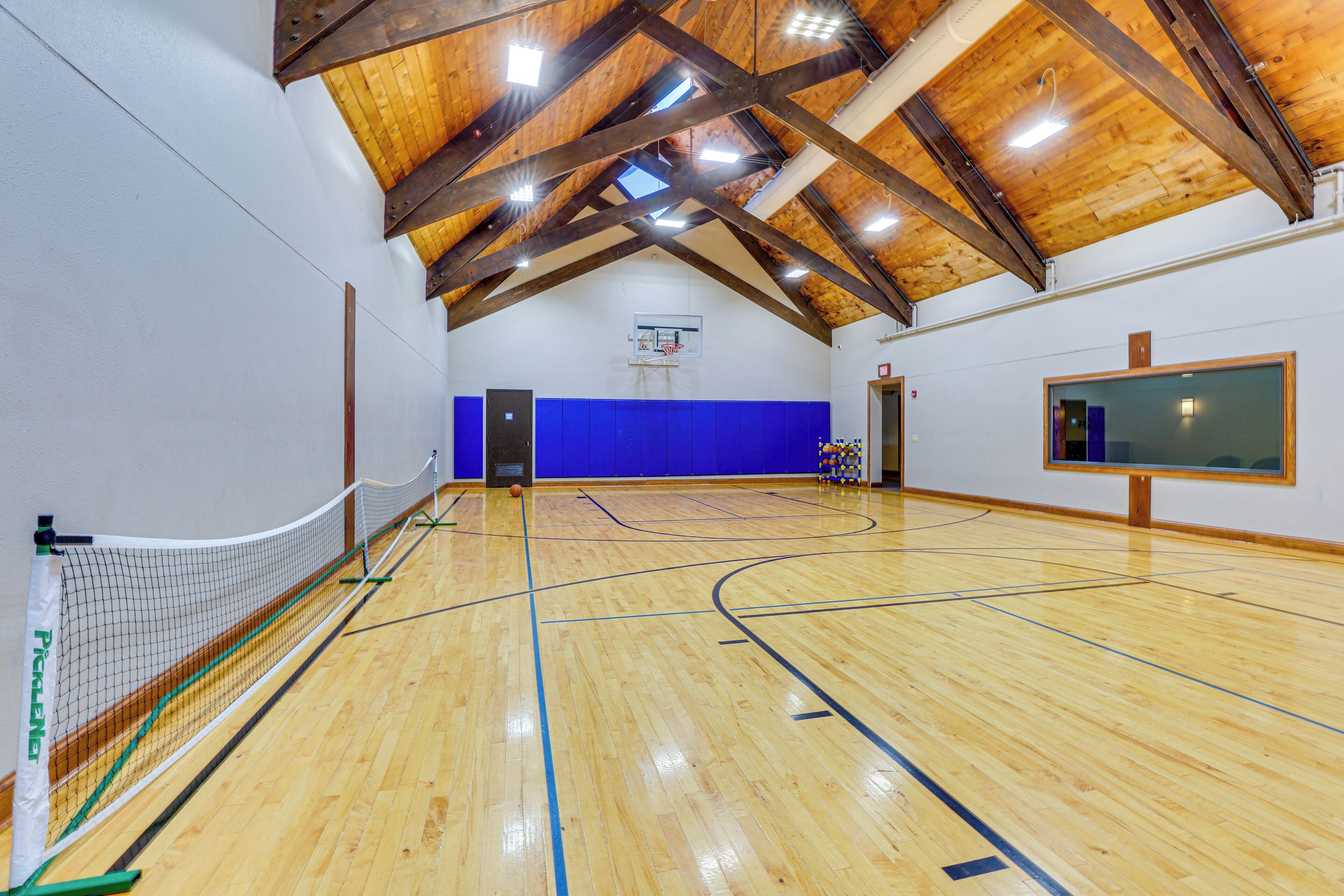 Una cancha de baloncesto interior con techo de madera y paredes azules acolchadas.