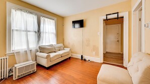 A living room with a beige sofa, a white radiator, and a television mounted on the wall.
