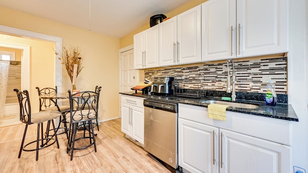 A modern kitchen with white cabinets, a dishwasher, and a tiled backsplash.