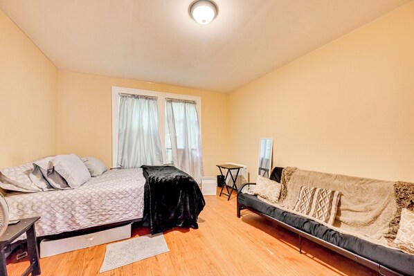 A bedroom with a bed, a sofa, a small table, and a radiator.