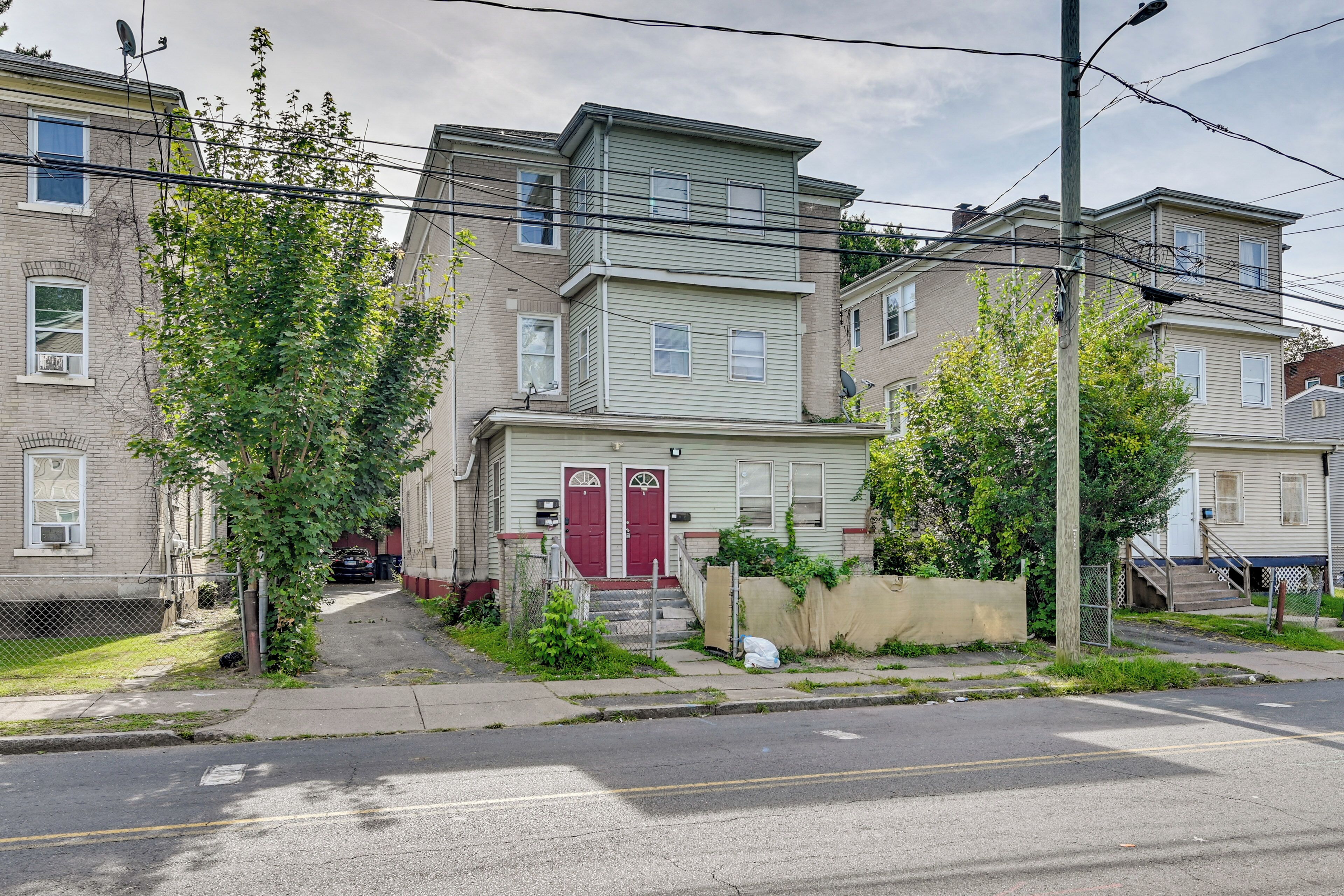 A row of townhouses with a central red door, a small front yard, and a sidewalk.