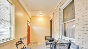 A narrow corridor with a small table and two chairs, a door, and a window with blinds.