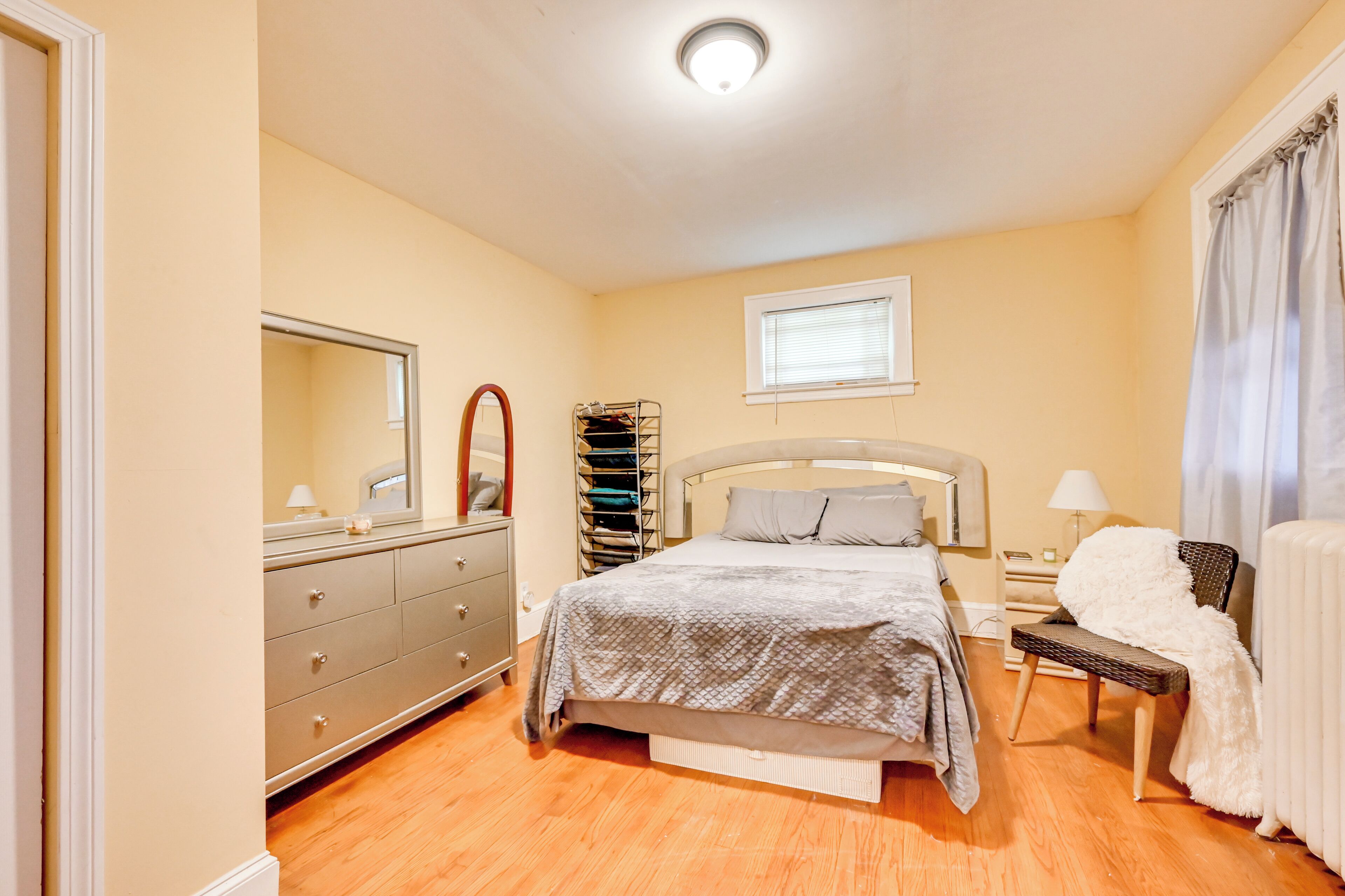 A bedroom with a bed, dresser, mirror, and a window with blinds.