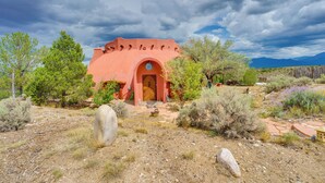 A rustic adobe building with an arched entrance, surrounded by desert vegetation and a clear sky. - Taos Dome Home w/ Hot Tub, Fireplace + Mntn Views! (Arroyo Hondo)