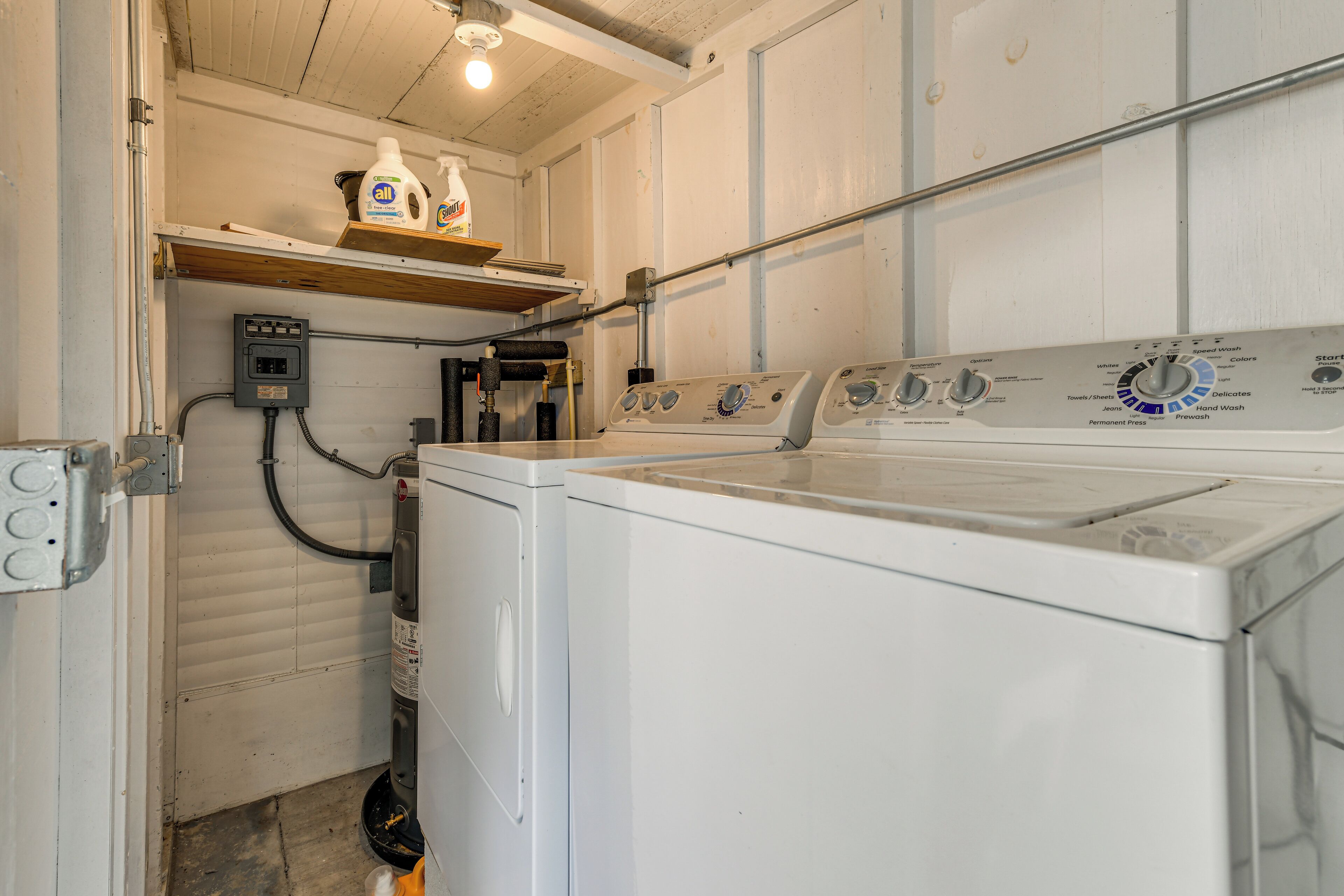 A laundry room with a front-loading washing machine, a dryer, and a shelf with cleaning supplies.