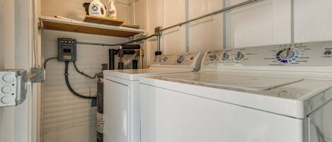 A laundry room with a front-loading washing machine, a dryer, and a shelf with cleaning supplies.