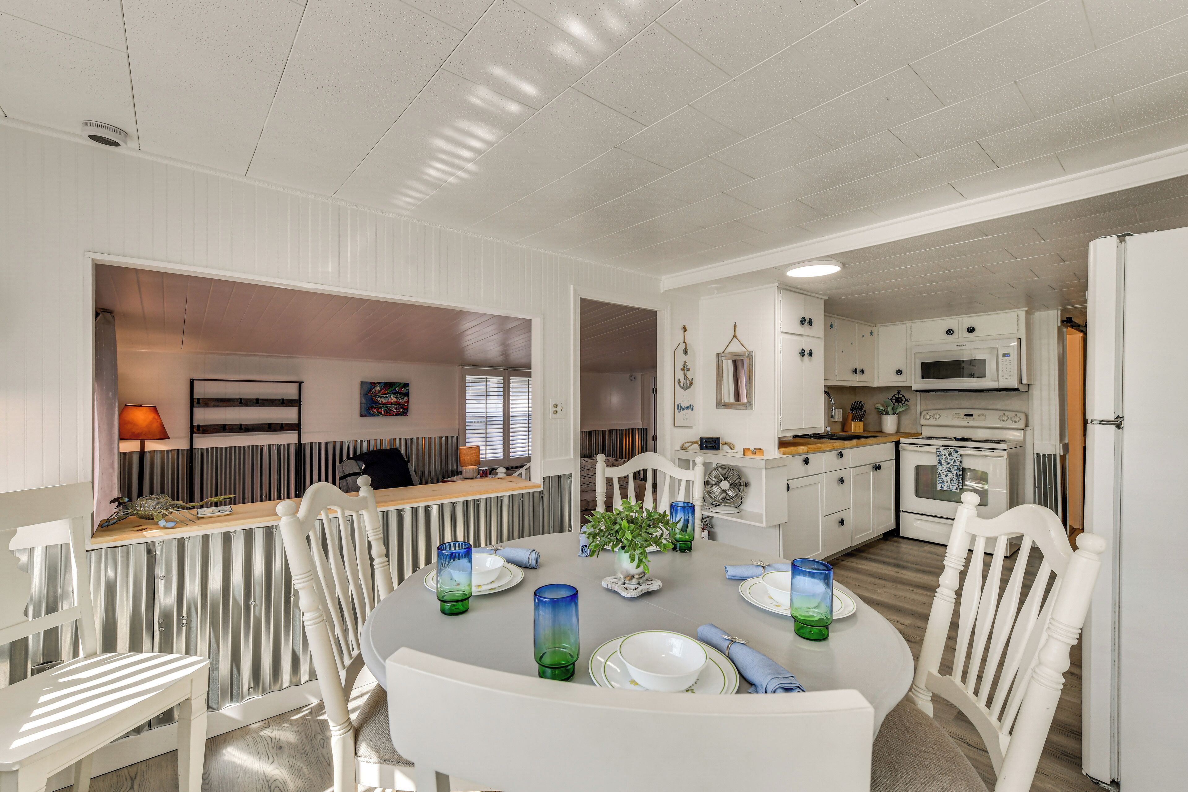 A dining area with a round table set for four, white chairs, and a kitchen in the background.