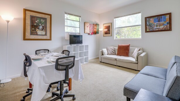 A living room with a dining table set for four, a gray sofa, a white couch, and a TV on a stand. - Walk to King Street Eats! Condo in Jacksonville (Jacksonville)