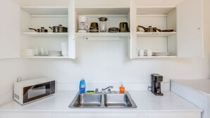 A kitchen with a microwave, double sink, and various kitchen items on shelves. - Walk to King Street Eats! Condo in Jacksonville (Jacksonville)