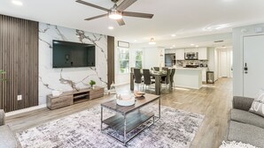 A modern living room with a marble wall, a ceiling fan, and a dining area with a kitchen in the background. - Florida Fun! Family Condo w/ Pool, 8 Mi to WDW (Kissimmee)