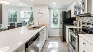A modern kitchen with a large island, stainless steel appliances, and a 'welcome' sign on the wall. - Florida Fun! Family Condo w/ Pool, 8 Mi to WDW (Kissimmee)