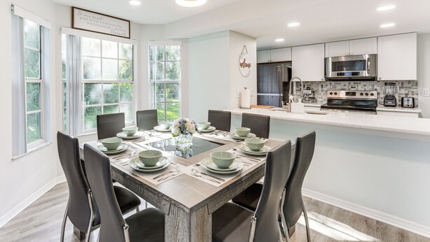 A modern kitchen with stainless steel appliances, a dining area with a wooden table and chairs, and large windows offering a view of greenery. - Florida Fun! Family Condo w/ Pool, 8 Mi to WDW (Kissimmee)