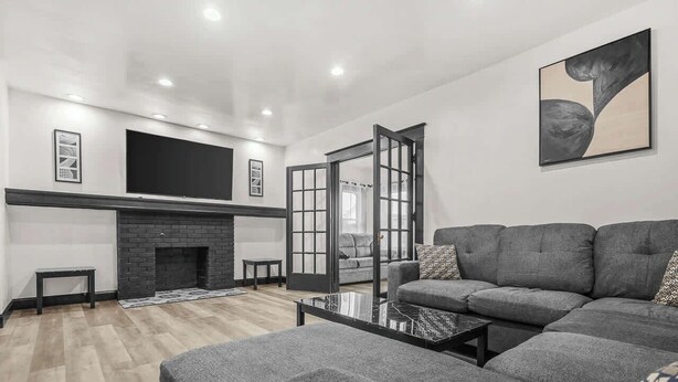 A modern living room with a fireplace, a large grey sofa, a flat-screen TV mounted on the wall, and a glass coffee table.