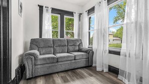 A gray sofa in a room with large windows and white curtains.