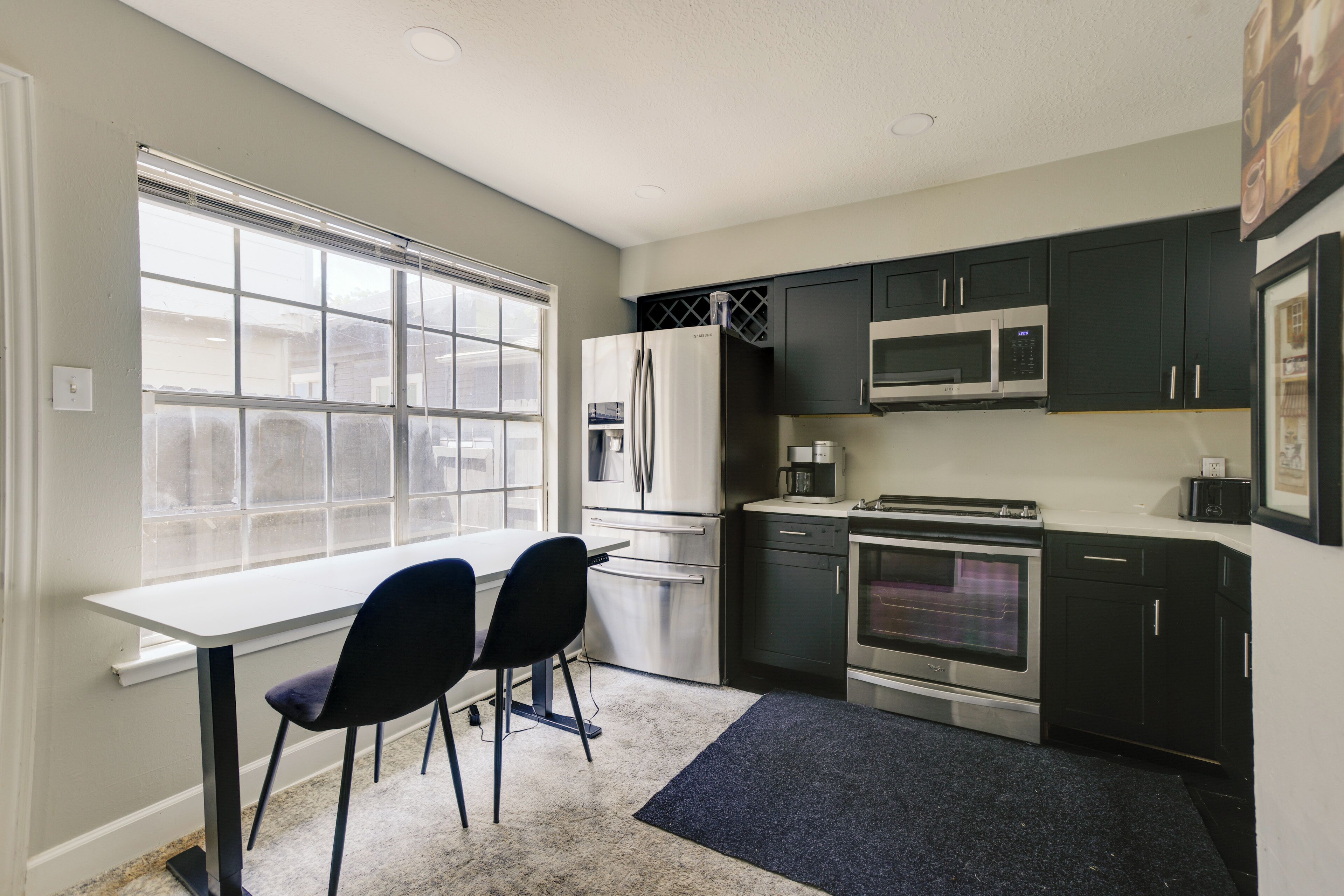 A compact kitchen with a window, stainless steel appliances, and dark cabinets.