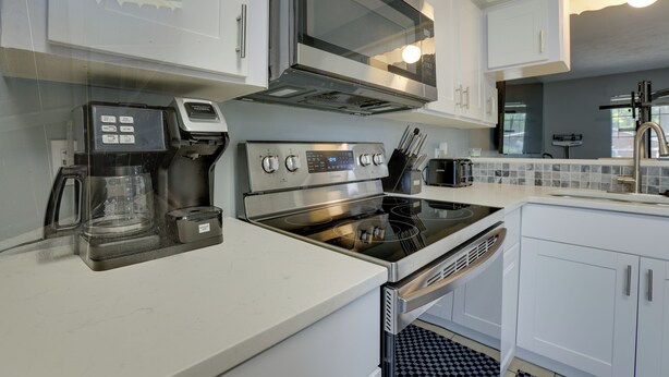 A modern kitchen with stainless steel appliances, white cabinetry, and a checkered floor pattern.