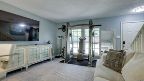 A living room with a large flat-screen TV, a sofa, a cabinet, and a weightlifting area.