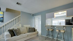 A living room with a sofa, two bar stools, a staircase, and a door leading to another room.