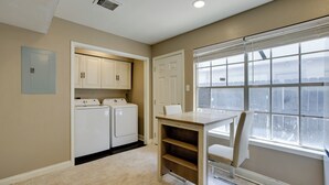 A laundry room with a washing machine and dryer, a table with a chair, and a window with blinds. - Near Airport & Interstate: Houston Area Townhome (Humble)