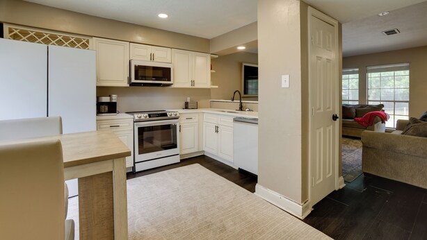 A modern kitchen with white cabinetry, a built-in microwave, and an oven. There is a dining area with a wooden table and chairs. - Near Airport & Interstate: Houston Area Townhome (Humble)