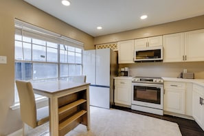 Una cocina con armarios blancos, horno empotrado, microondas y refrigerador.