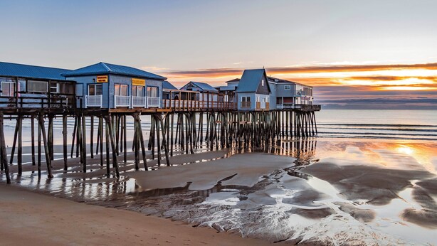 A waterfront property with multiple buildings on stilts, connected by a wooden deck. - Modern Gem on 15 Acres, 5 Mi to Old Orchard Beach! (Saco)