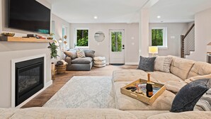 A modern living room with a fireplace, a large TV, and a cozy seating area with a tray of drinks. - Modern Gem on 15 Acres, 5 Mi to Old Orchard Beach! (Saco)