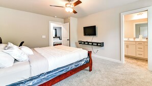A bedroom with a bed, a ceiling fan, a mounted TV, and a bathroom visible through an open door.
