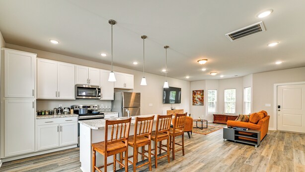 A modern kitchen with white cabinets, stainless steel appliances, and a wooden dining area.