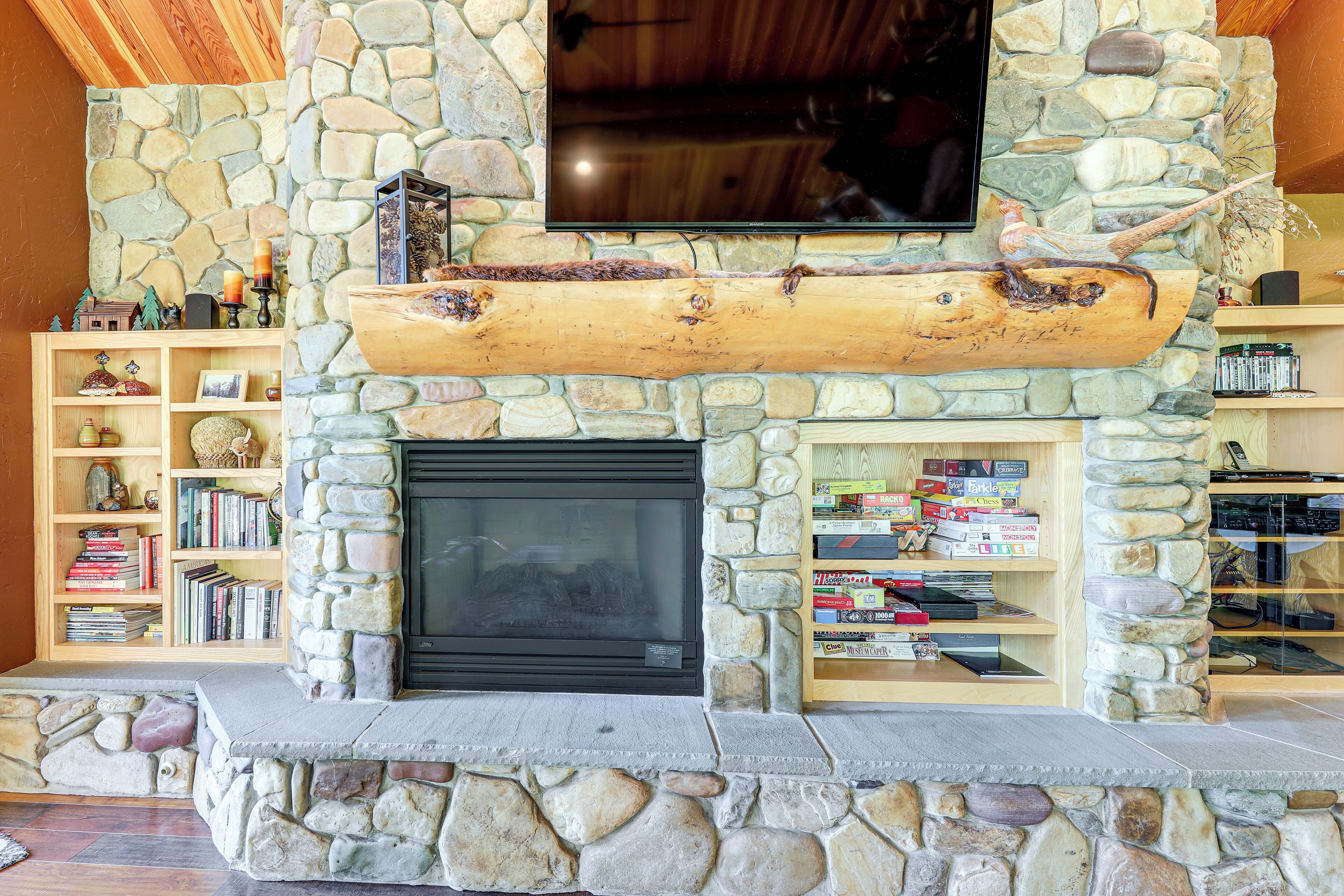 A stone fireplace with a log shelf above, surrounded by bookshelves filled with books and decorative items.