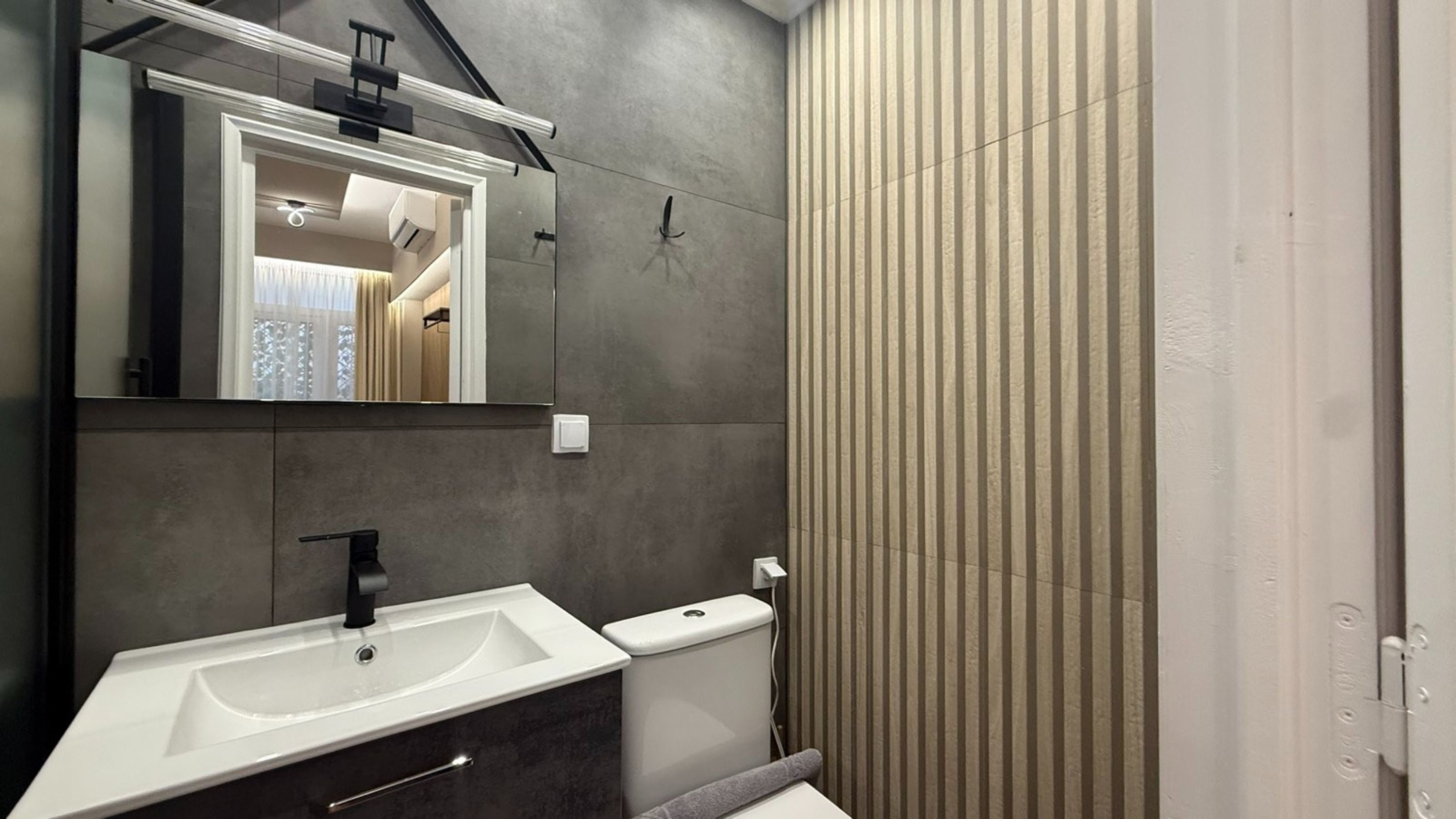 Une salle de bain moderne avec un grand miroir, un lavabo blanc et des toilettes.