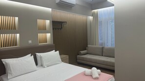 Moderni hotellihuone, jossa on suuri sänky, sohva ja ikkuna, jossa on verhot.