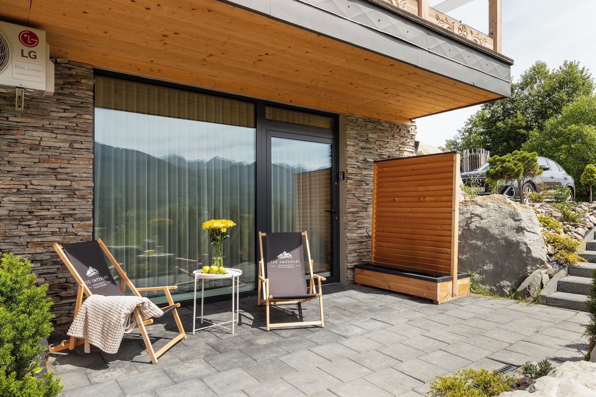 Un espacio exterior moderno con dos sillones de relax, una mesita con un florero y una pared de piedra.