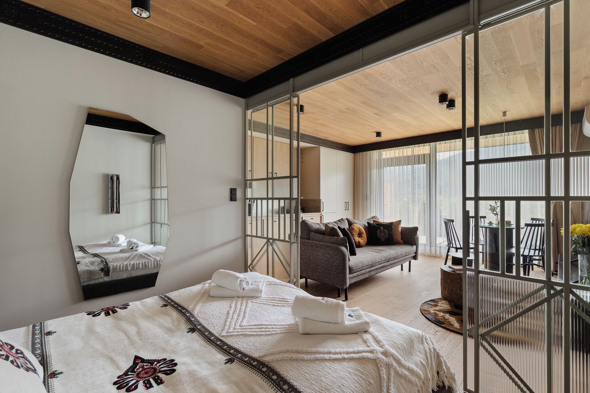 A modern hotel room with a large bed, a sofa, a dining area, and a balcony with a view.