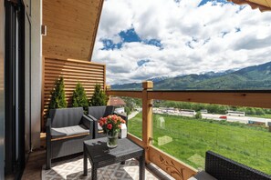 A balcony with wicker furniture, a vase of flowers, and a view of green fields and mountains. - IJG Imperial Apartamenty Szymaszkowa (Zakopane)