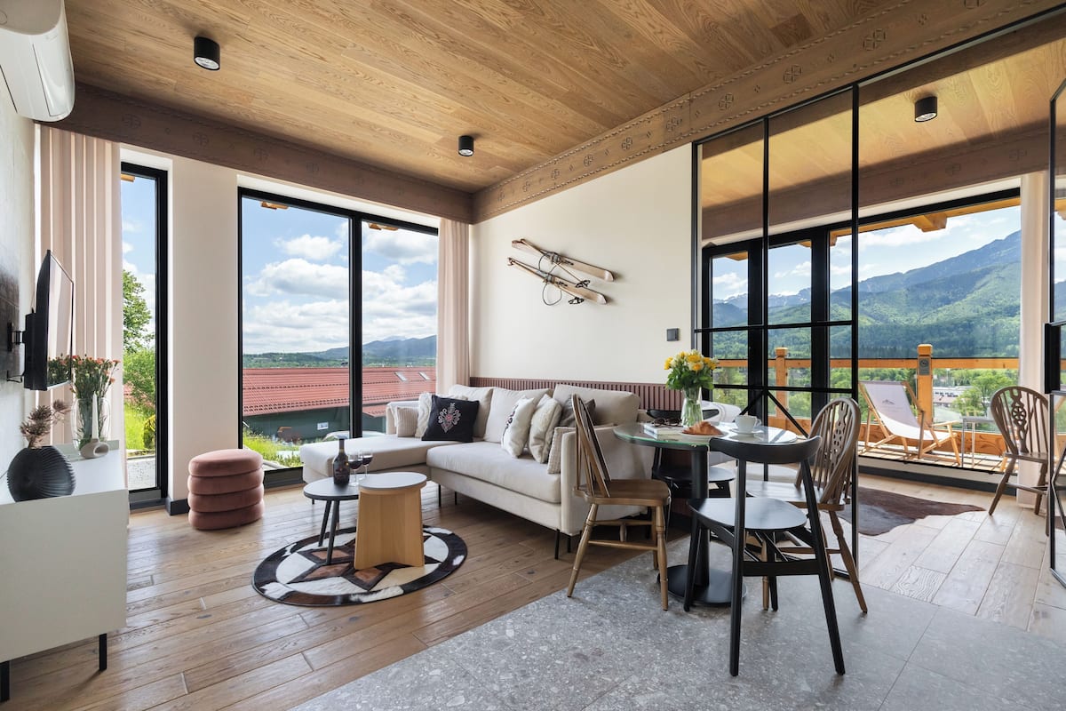 A spacious living area with a large window offering a mountain view, a cozy seating arrangement, and a ski rack on the wall.