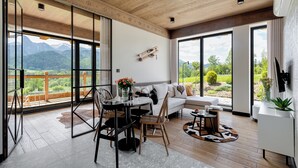 A modern living room with a wooden ceiling, large sliding glass doors, a white sofa, a dining table, and a view of mountains. - IJG Imperial Apartamenty Szymaszkowa (Zakopane)