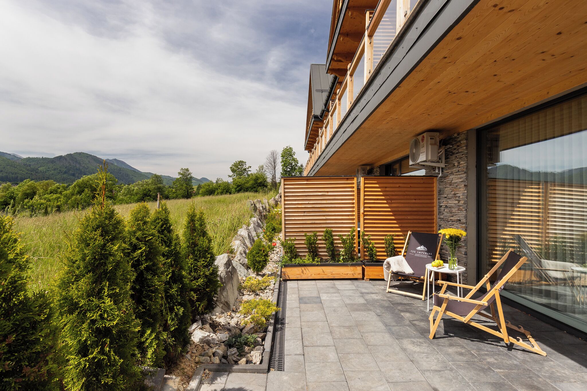 A modern house with a wooden exterior, a stone wall, and a patio with outdoor furniture.