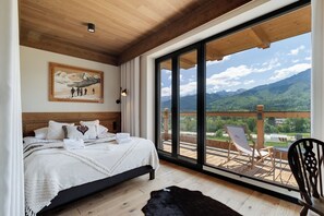 A bedroom with a large bed, a painting on the wall, and a balcony with chairs and a view of mountains. - IJG Imperial Apartamenty Szymaszkowa (Zakopane)