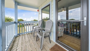 A covered porch with a view of the beach, two Adirondack chairs, and a sliding glass door. - The Cove Condos (Gulf Shores)