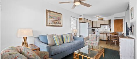 A living room with a sofa, armchair, coffee table, and a ceiling fan.