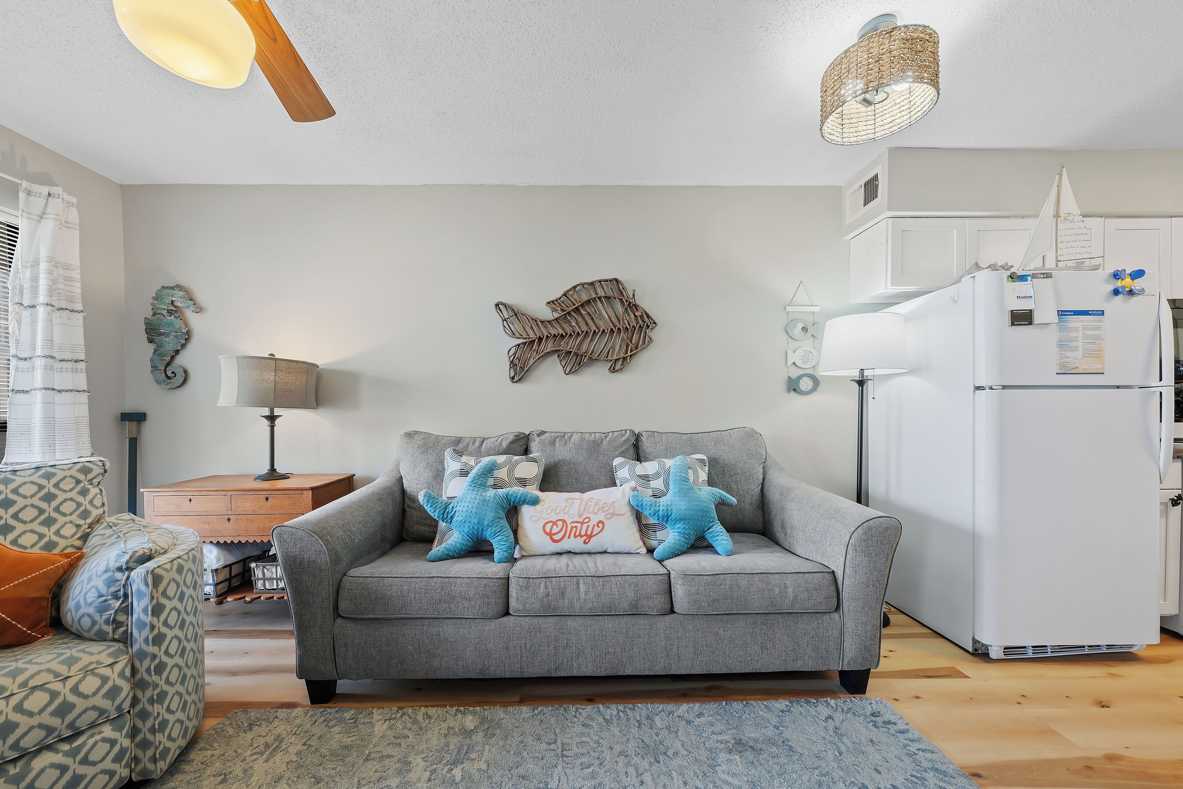 A modern living room with a grey sofa, decorative pillows, a wooden side table, a lamp, and a wall-mounted fish decoration.