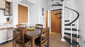 A dining area with a wooden table and chairs, a kitchen with a sink, and a spiral staircase. - The Cove Condos (Gulf Shores)