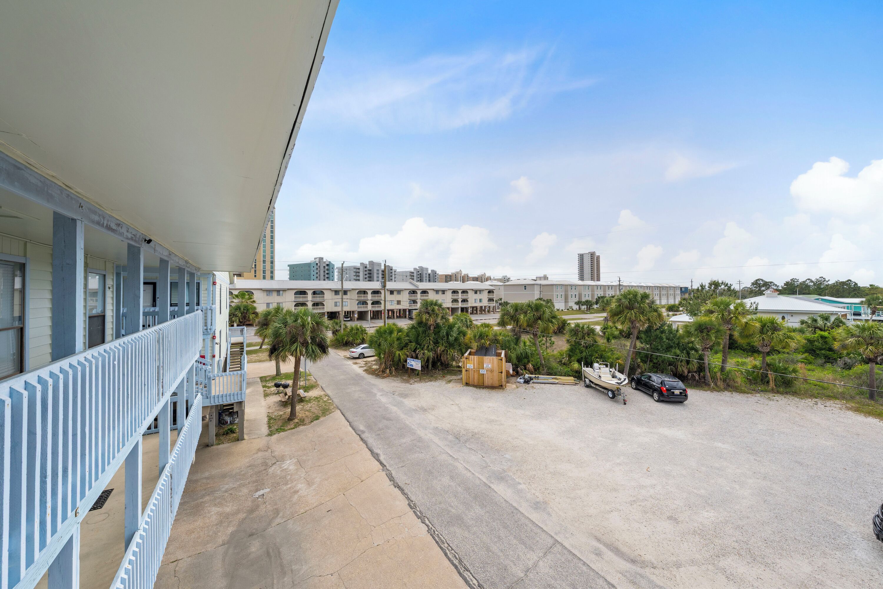 Un hotel con un área exterior cubierta, estacionamiento y vistas de edificios y palmeras circundantes.