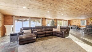 A cozy living room with a sectional sofa, a fireplace, and a view of a snowy landscape through large windows. - Updated 4BR, Game Room/Bar, Private, Near Gunstock (Gilford)